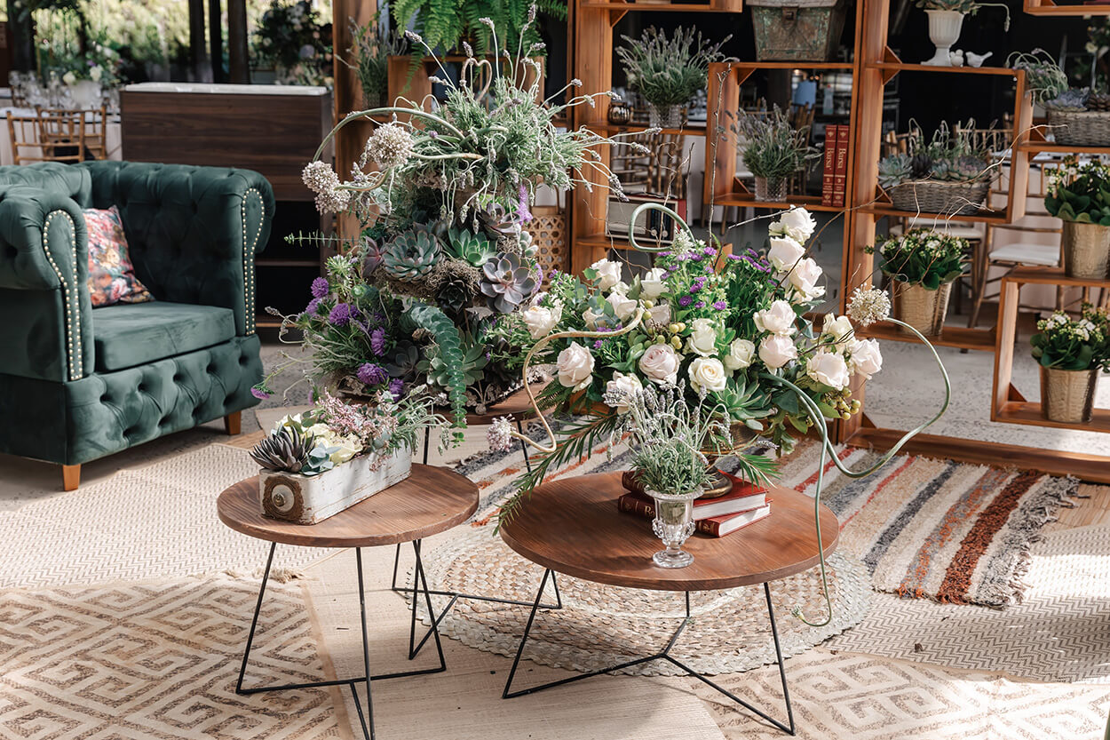 lounge com sofás verdes e mesas redondas no centro vaos de flores brancas e lavandas