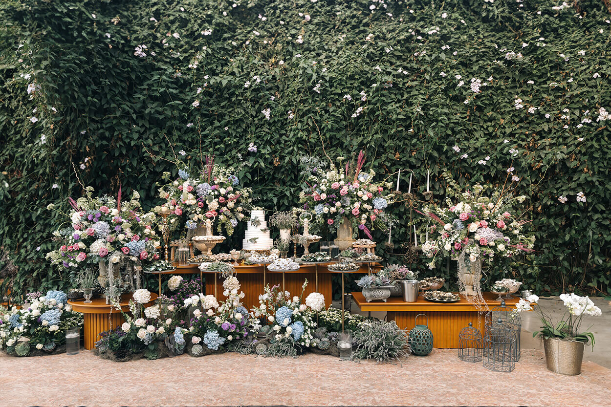 três meses de madeira com bolo de casamento branco com três andares com lavandas no topo e vasos com flores azuis brancas rosas e lilás