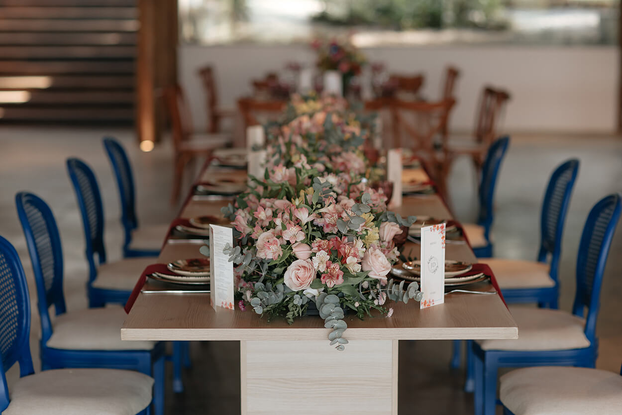 cadeiras azuis mesa posta com guardanapos na cor marsala e centro de mesa com folhas de eucalipto e rosas 