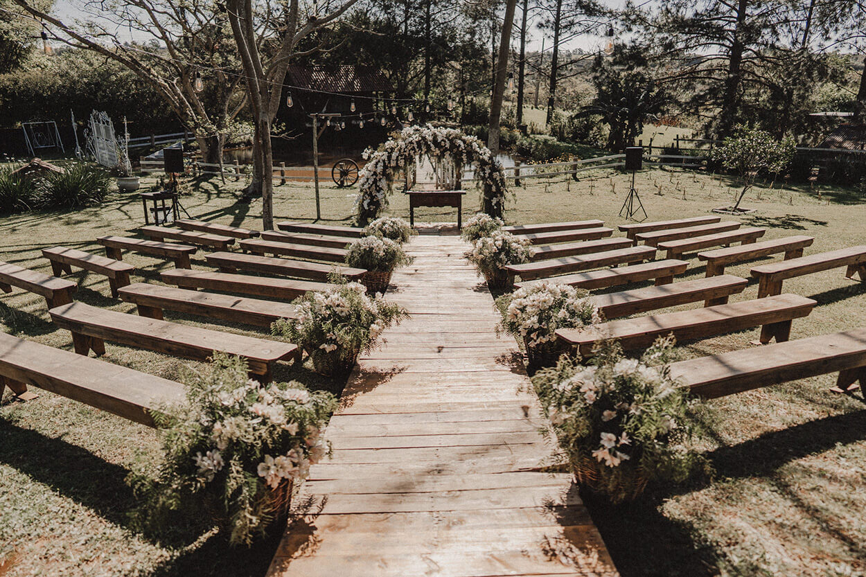 bancos de madeira decorados com flores brancas e altar com flores brancas no campo