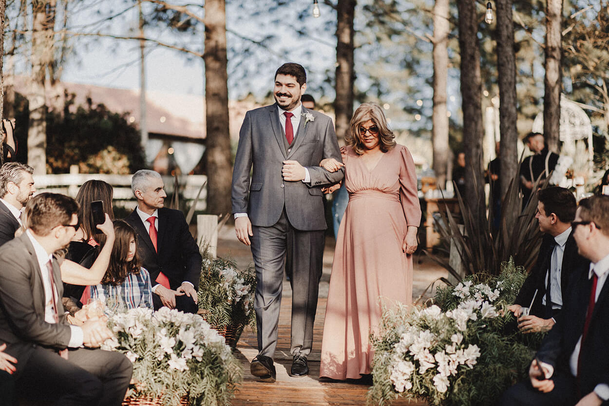 entrada do noivo com tenro cinza gravata vermelha ao lado da mãe com vetsido rose