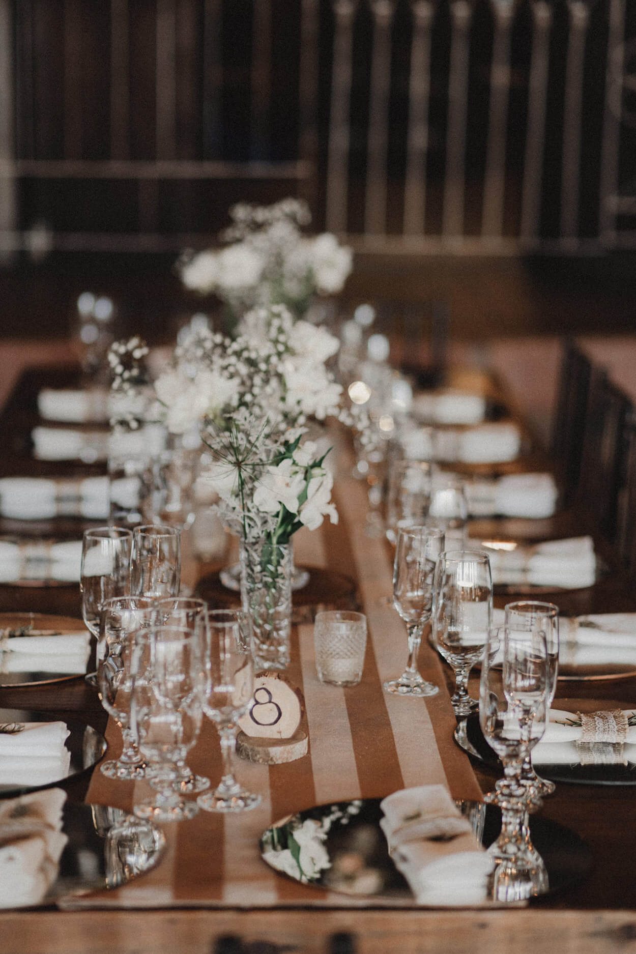 mesa posta com tecido marrom listrado e flres brancos em vasos de vidro no centro