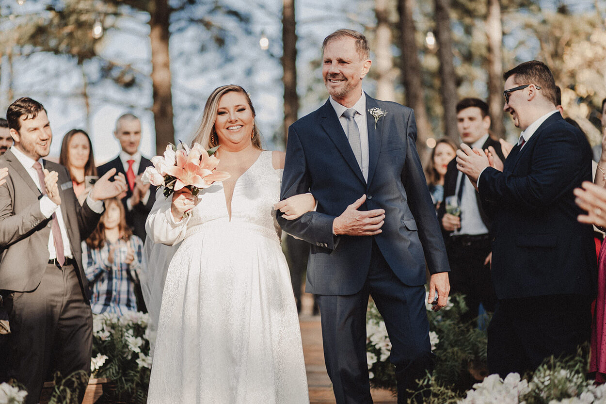 entrada da noiva com buquÊ rosa e branco ao lado do pai com terno azul escuro