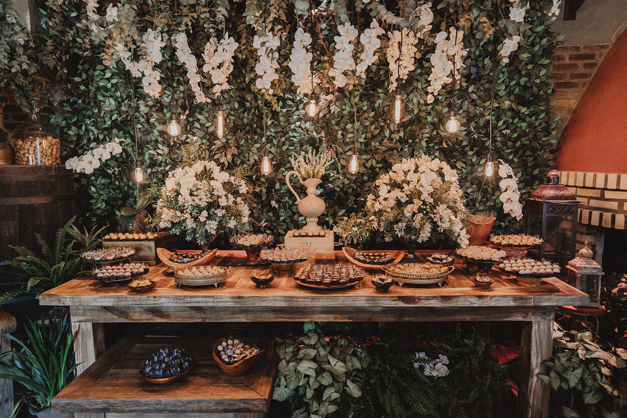 mesa de madeira rústica com bandejas de madeira com doces de casamento e vaoss com flores brancos