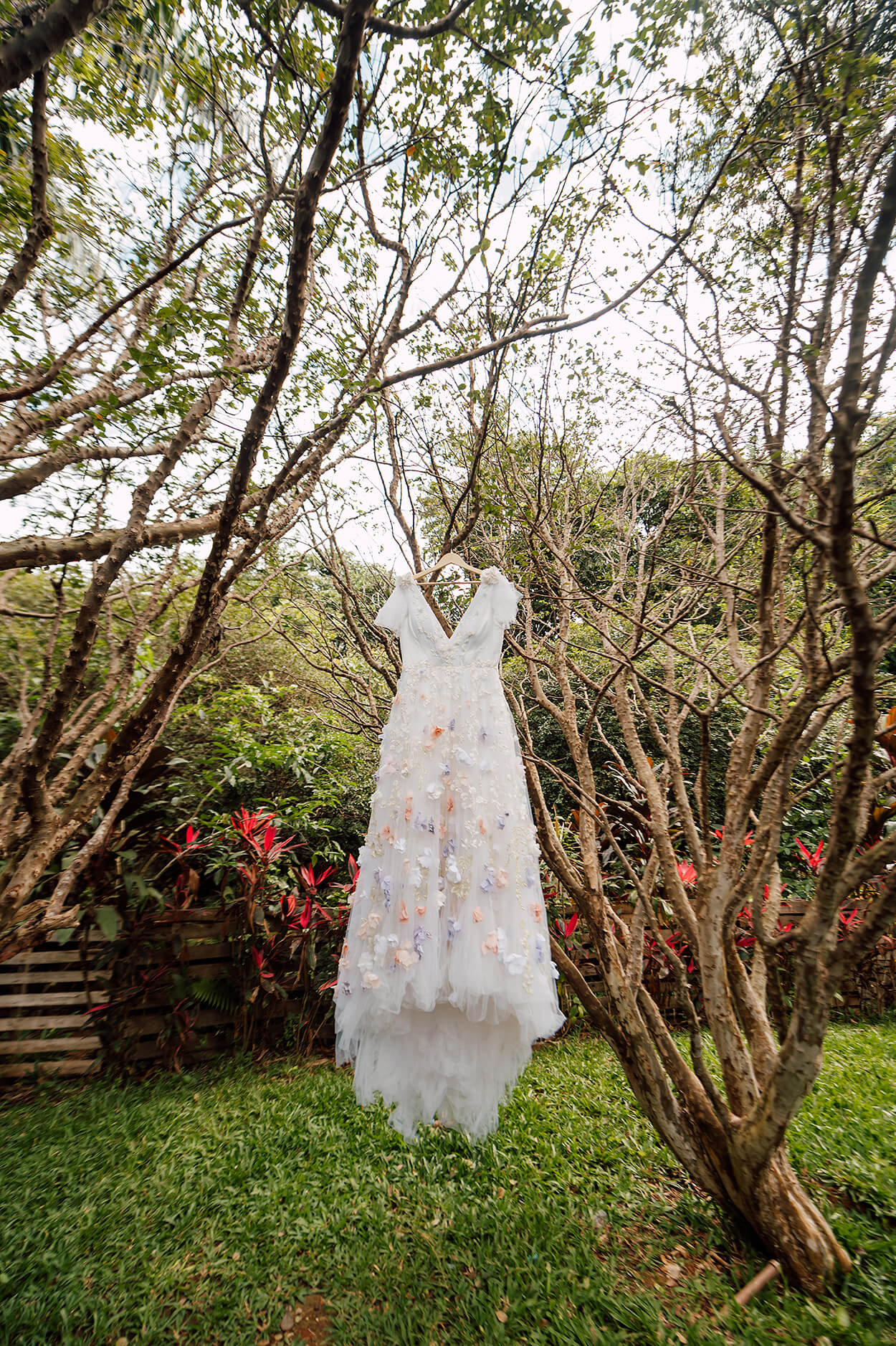 vestido de noiva com aplicação de flores coloridas pendurado em árvore no jardim