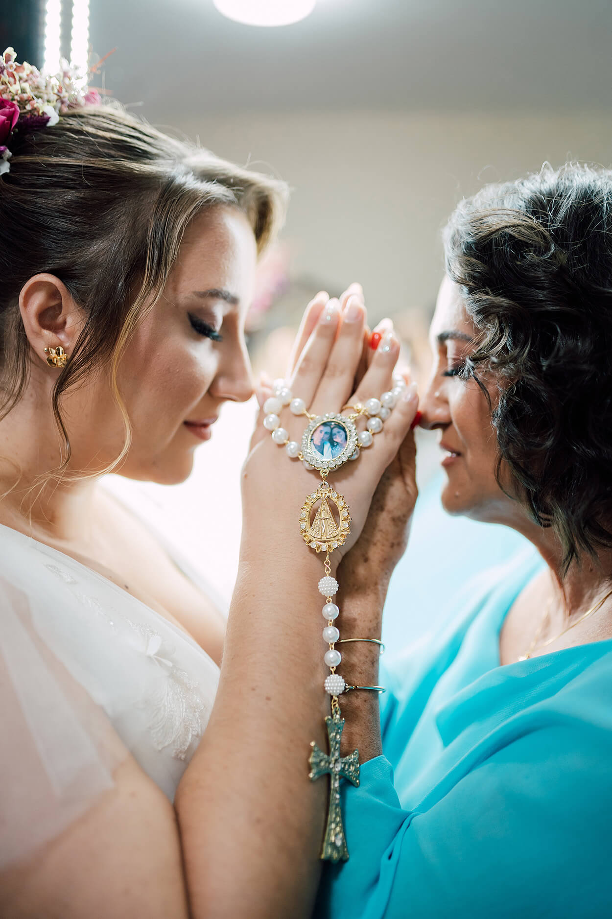 noiva e sua mãe com vestido auzl turquesa de olhos fechados orando com terço na mão