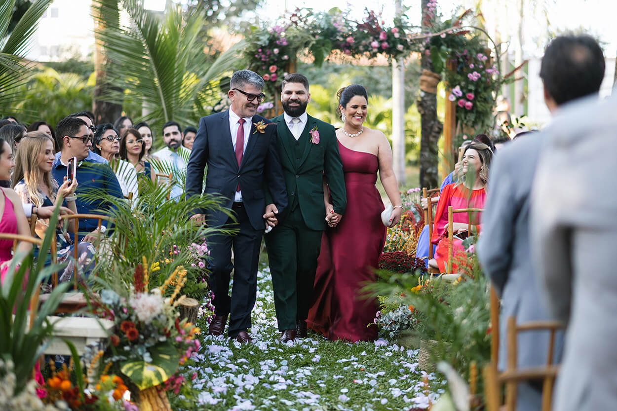 entrada do noivo com tenro verde escuro ao laod do pai com terno preto e gravata marsala e mãe com vestido marsala