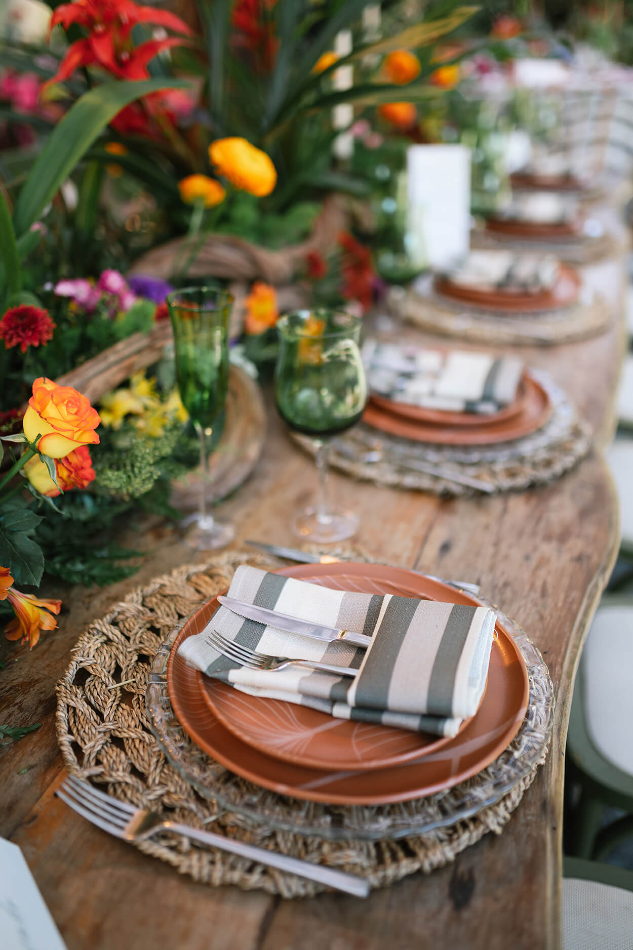 mesa posta com souplat rústico e guardanapo listrado e arranjo com flores no centro