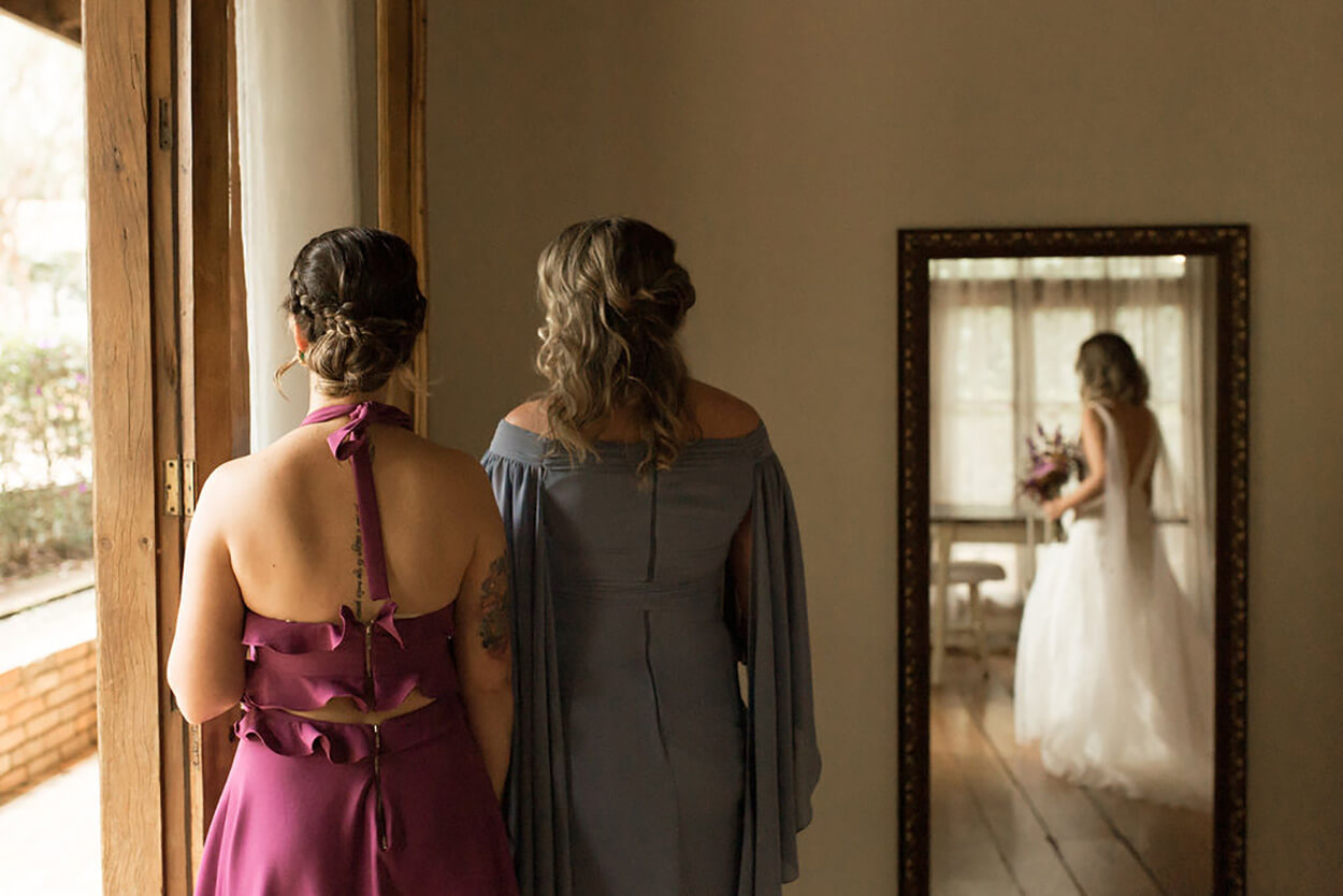 duas mulheres de costas e relfexo de noiva no espelho