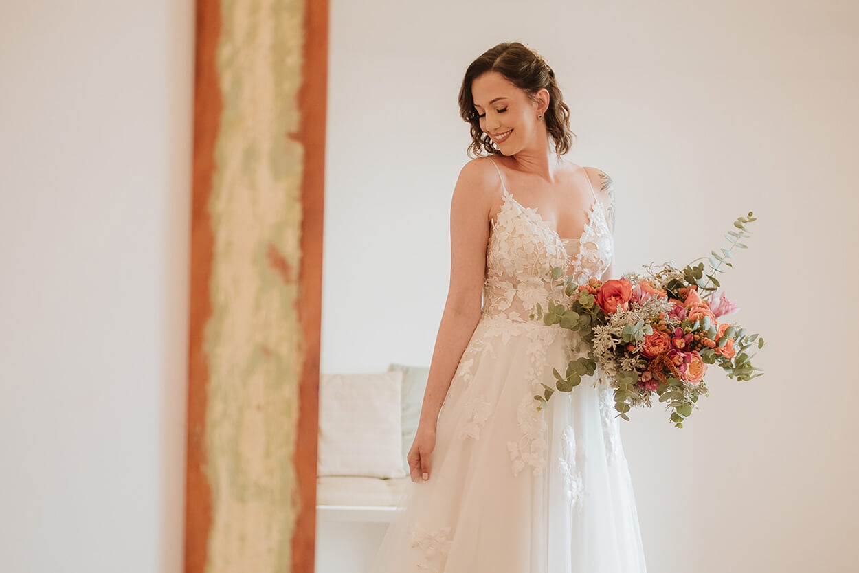 noiva com vestido com decote em v floral segurando buquê desconstruído com flores laranjas e rosas