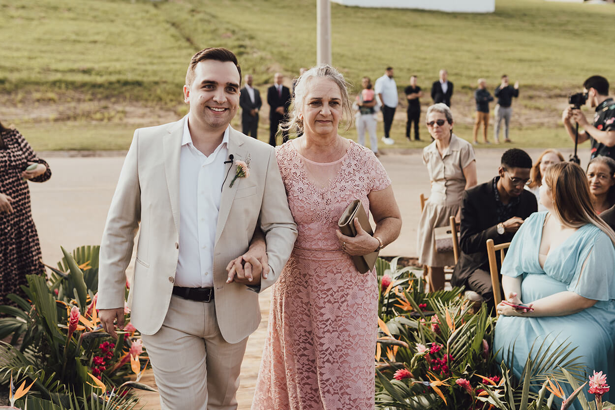 entrada do noivo com terno bege claro ao lado da mãe com vetsido rosê rendado longo