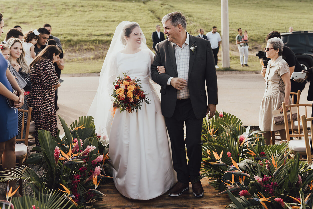 entrada da noiva com vetsido longo e minimalista com véu ao lado do pai com terno preto