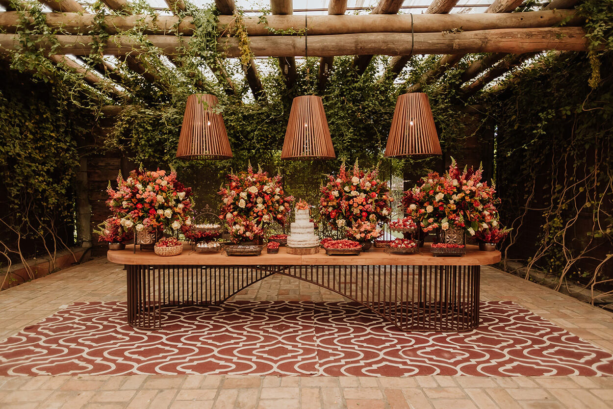 salão rústico com mesa de madeira com bolo de casamento semi espatulado e arranjos com flores terracota 