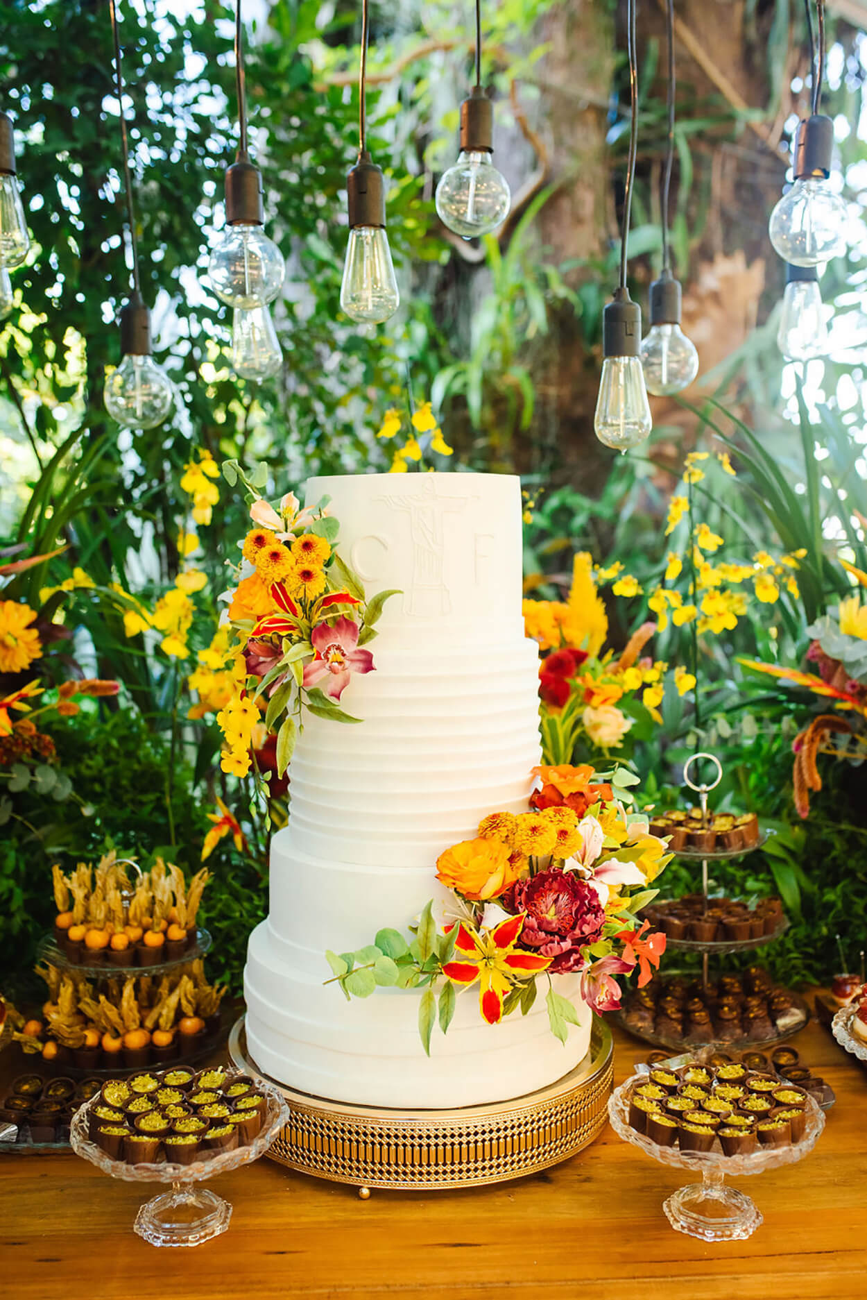 mesa de madeira com bolo de casamento branco com tres andares e arranjos com flores amarelas e vermelhas