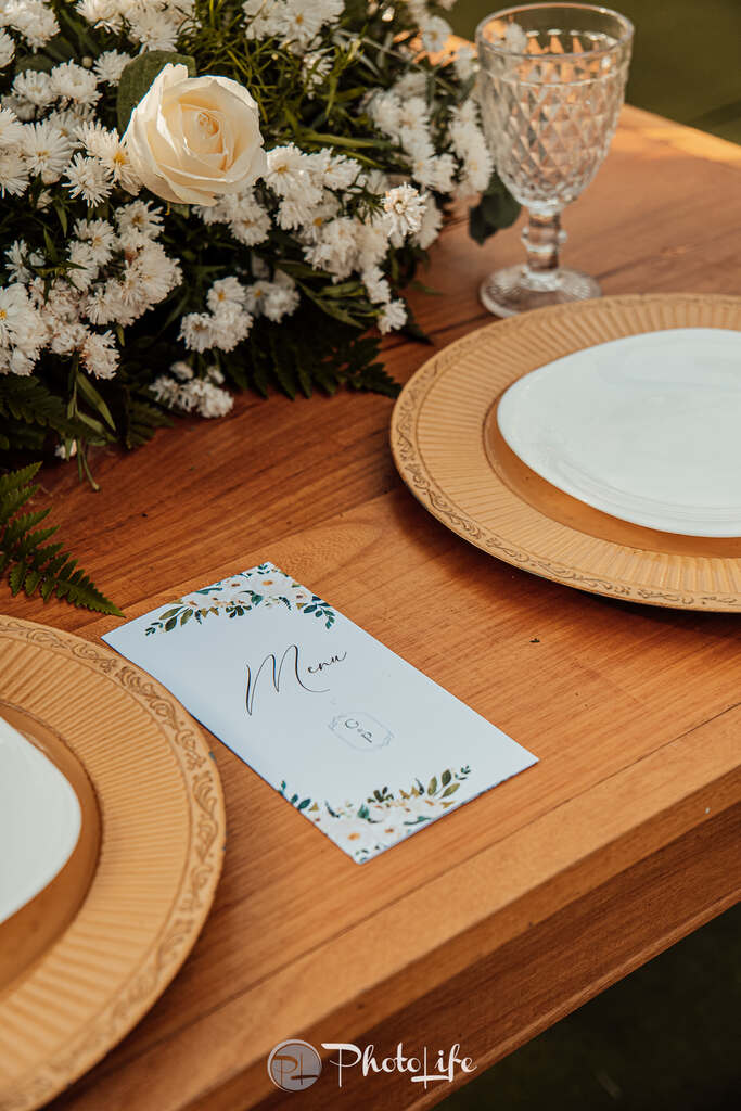 mesa de madeira com sousplat marrom e menu branco com ilustração de flores