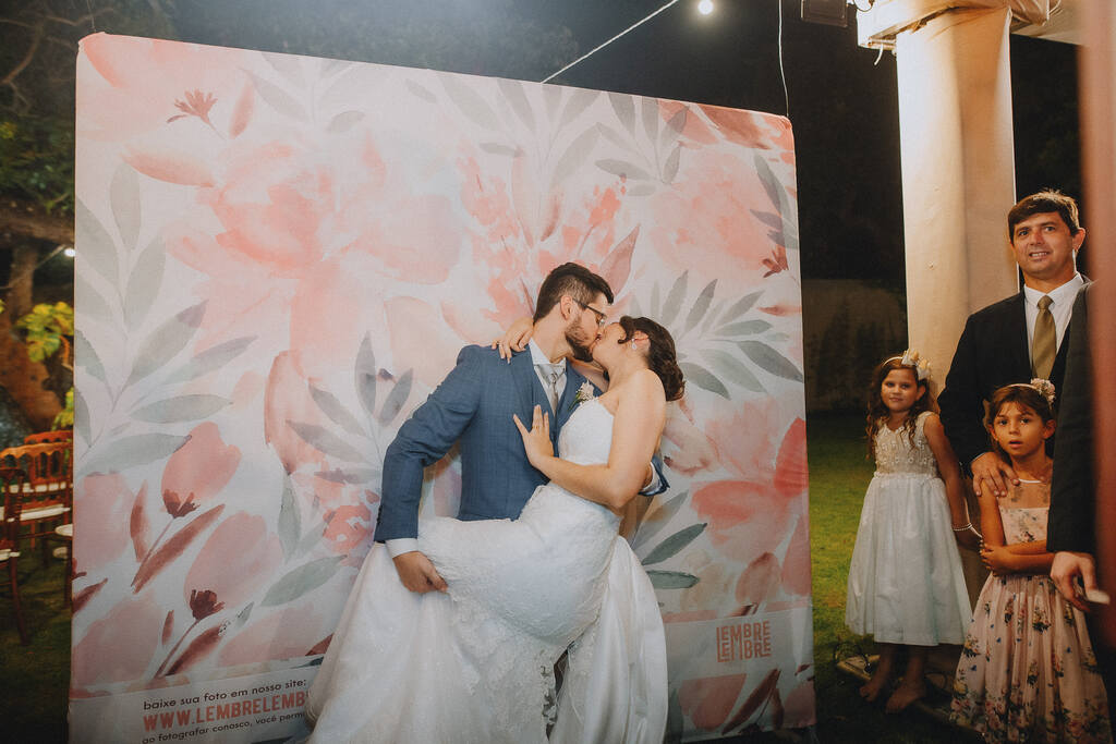 noivos se beijando na frente de backdrop com estampa de flores