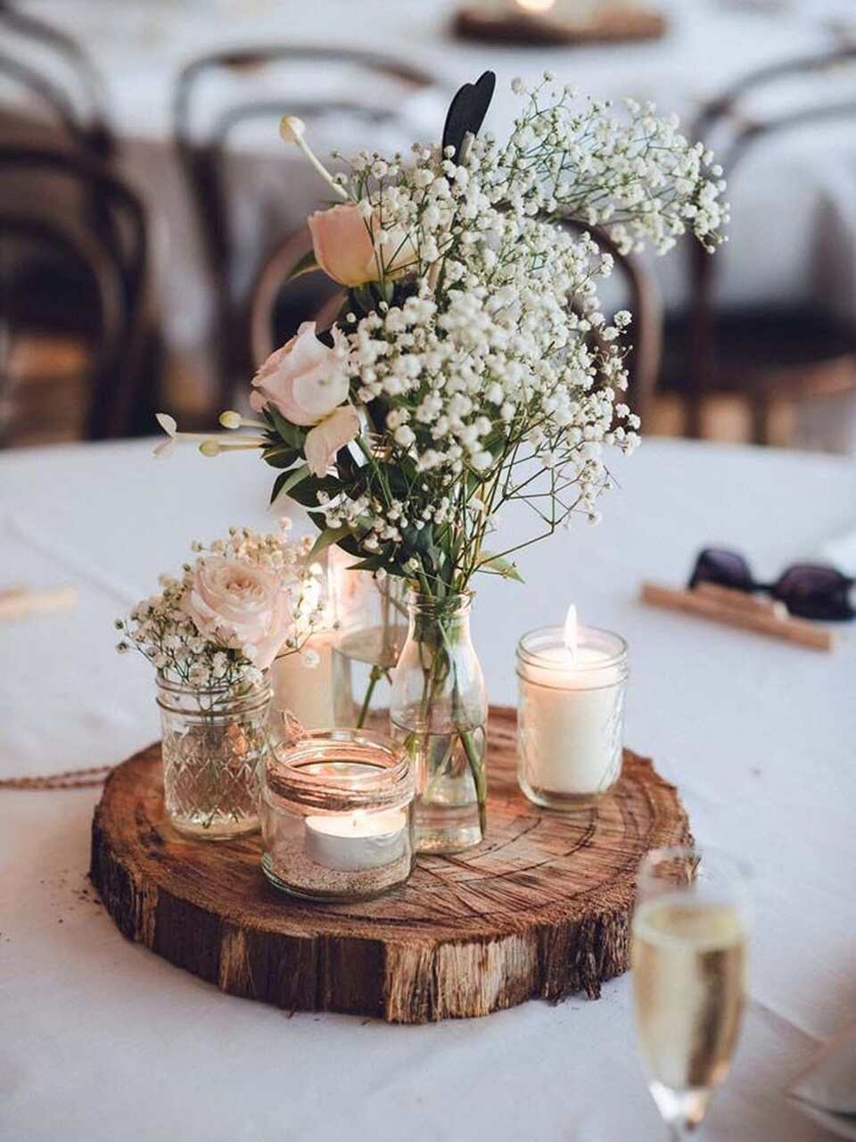 centro de mesa feito com rodela de madeira e copos transparentes com velas e arranjo com flores brancas