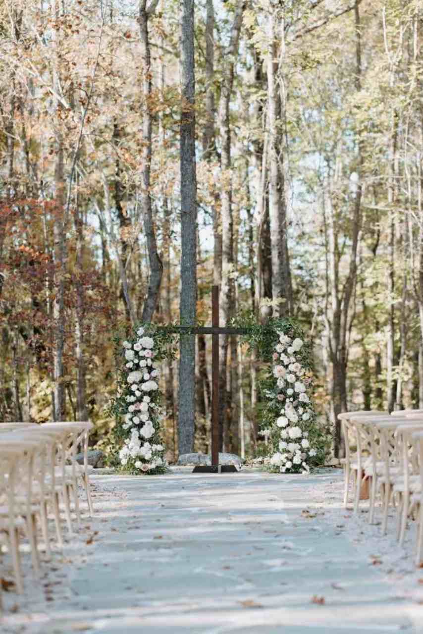 cruz de madeira no altar com arranjos florais brancos de frente para a floresta