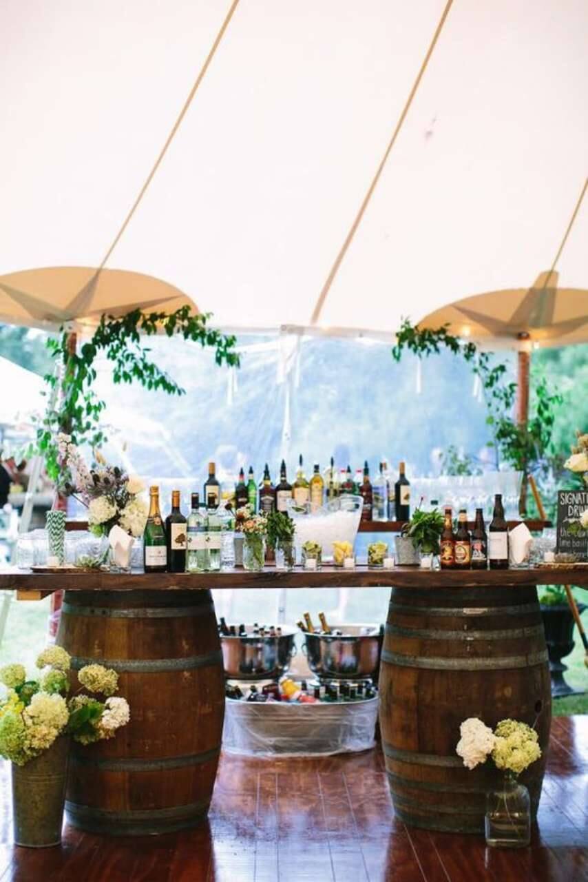 mesa de bar com bebidas feita com dois barris de madeira escuro