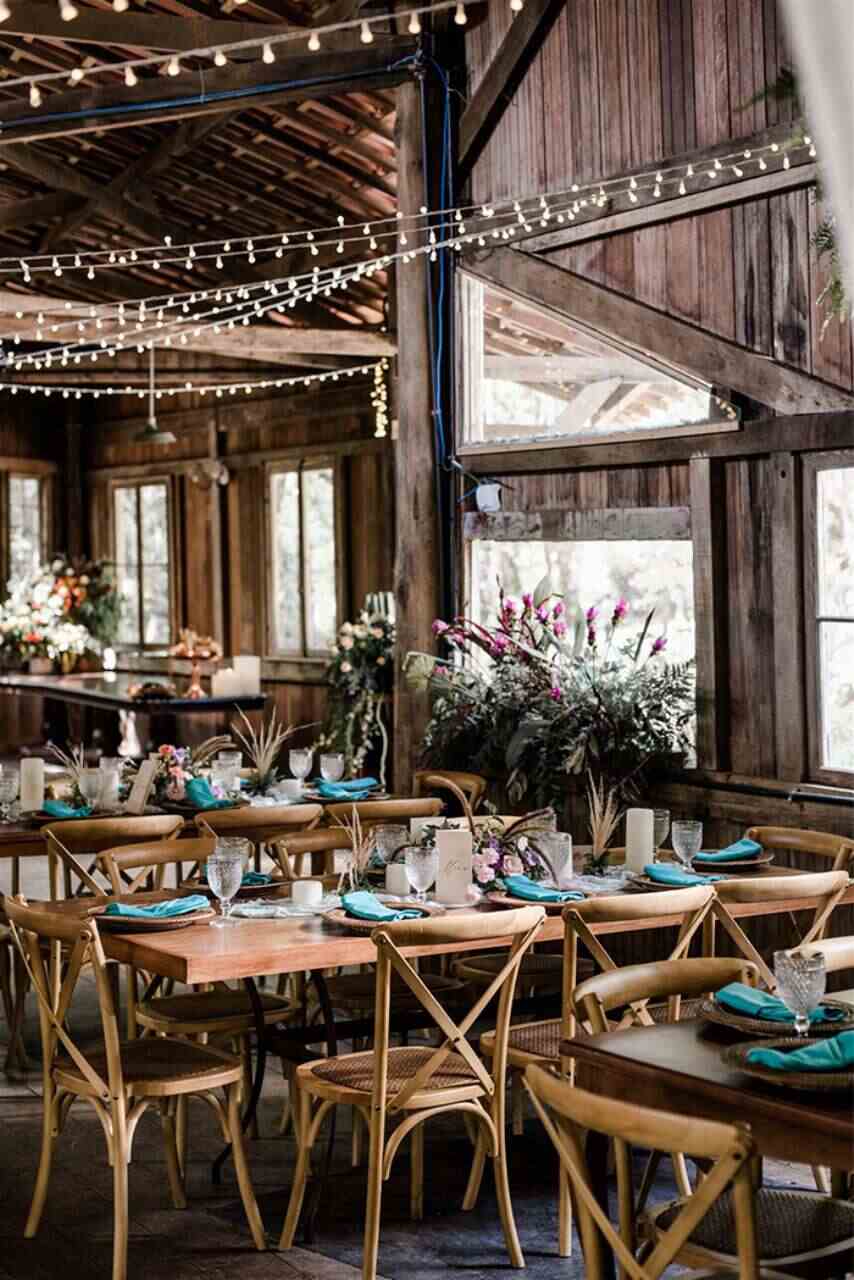 mesas de madeiras postas com guardanapos azul celeste em salão de madeira rústico com varal de luzinhas