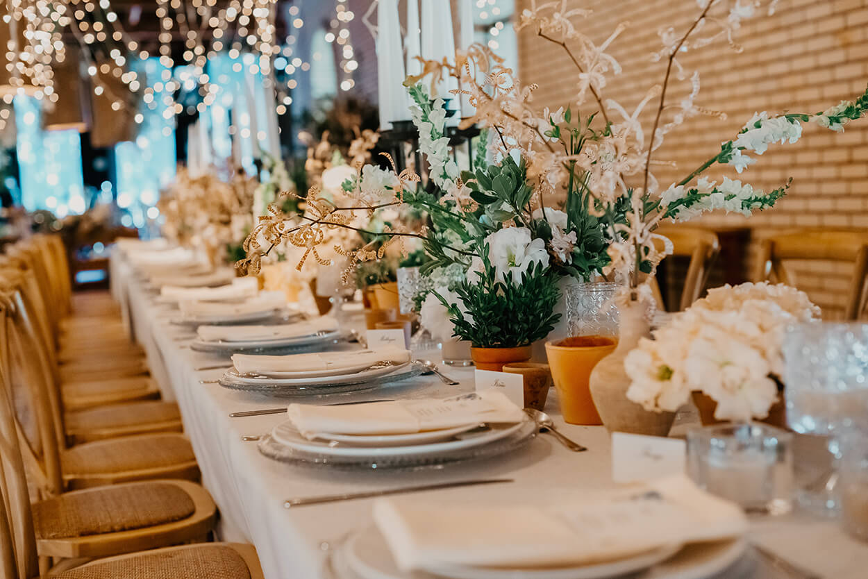 mesa posta com toalha branca e vasos com flores mosquitinhos