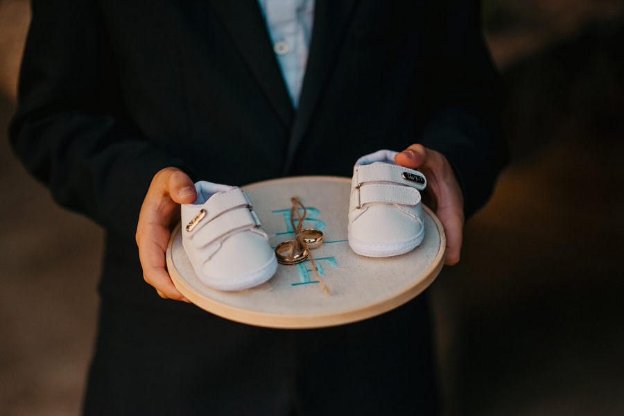 menino segurando porta aliança no bstidor bordado com sapatinho de bebê branco