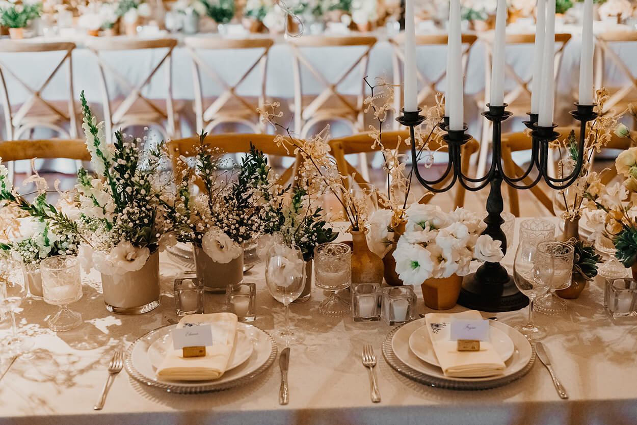 mesa posta com toalha branca e vasos com flores mosquitinhos