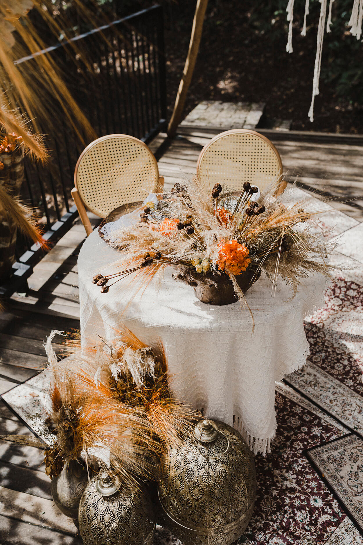 mesa redondad com toalha branca com arranjos com flores laranjas e cadeira com encosto com palhinha
