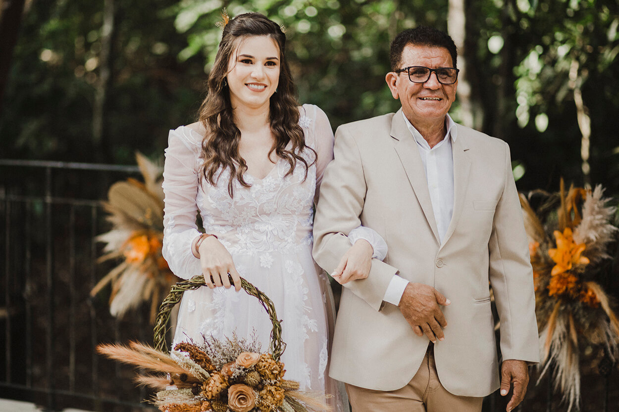entrada da noiva segurando hoop bouquet ao lado do pai com terno off white