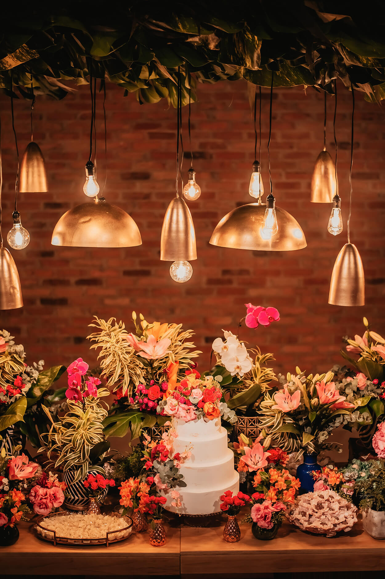 mesa de madeira com bolo de casamento com quatro andares com flores no topo e vasos com flores rosas ao lado