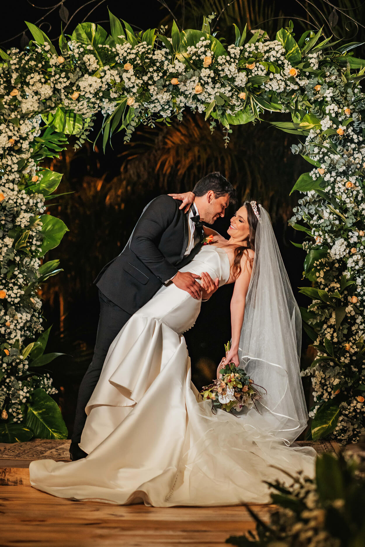 noivos beijando a noiva debaixo do arco de flores