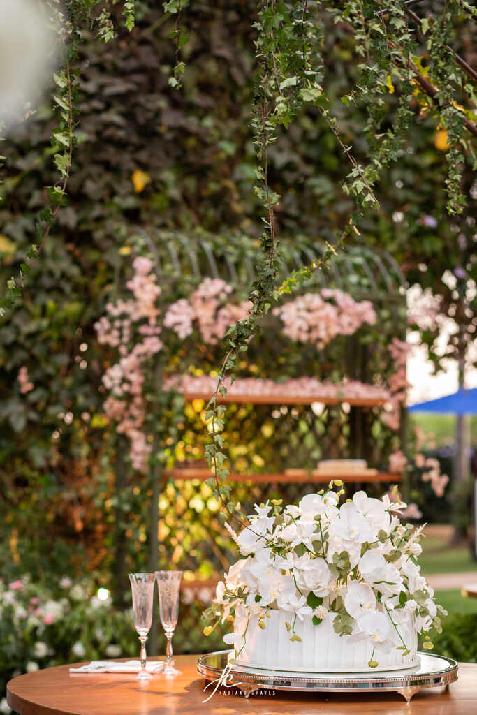 mesa de madeira com bolo de casamento branco com dois andares com topo de flores brancas