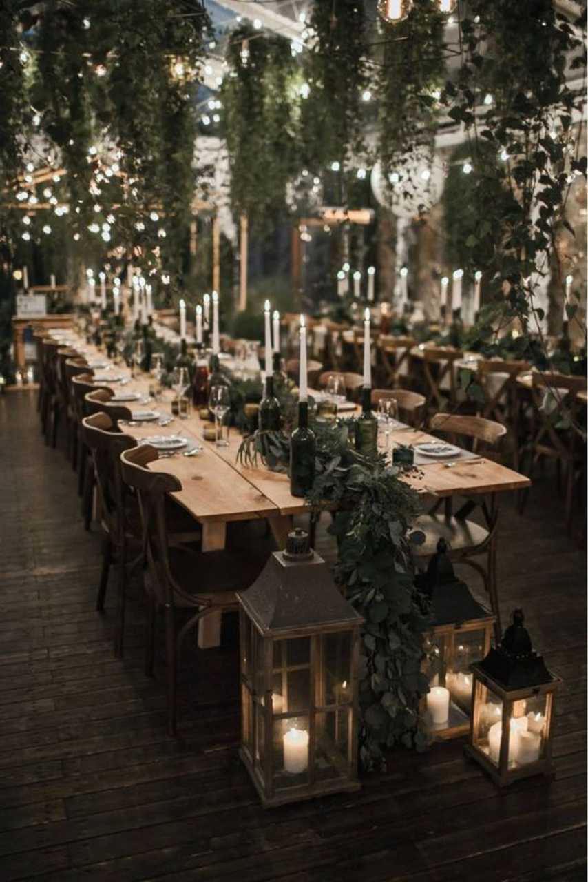 salão com mesas de madeira decoradas com velas e folhagens no centro
