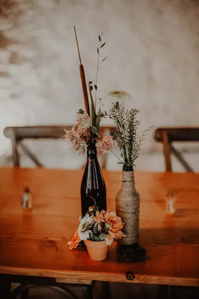 garrafas enroladas em sisal e arranjos de flores para centro de mesa de casamento rústico