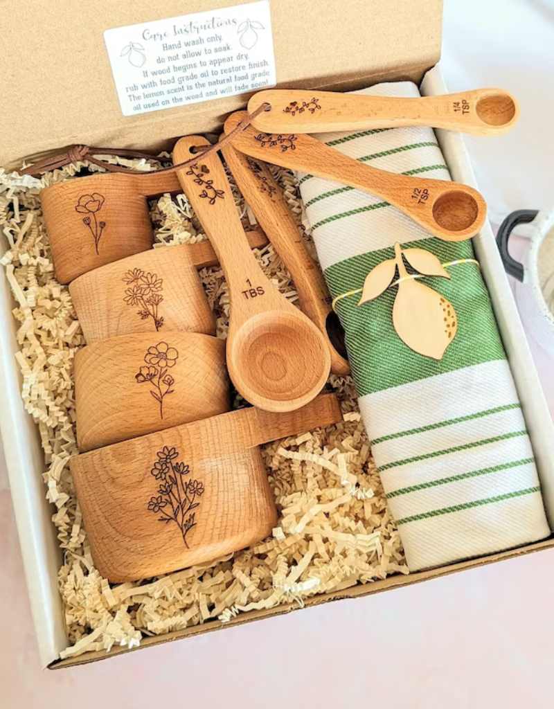 caixa de papelão com kit contendo xícaras e colheres medidoras em madeira + pano de prato para lembrancinha de chá de cozinha