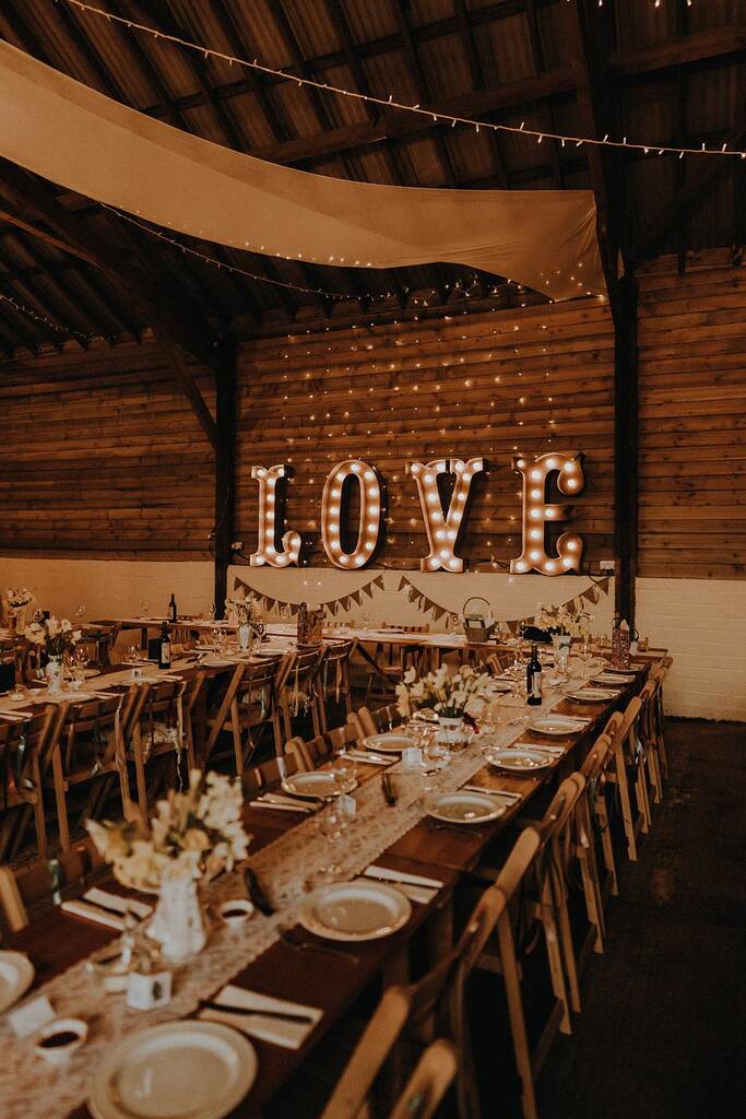 centro de mesa em renda e arranjos de flores. No espaço tem um letreiro neon escrito love