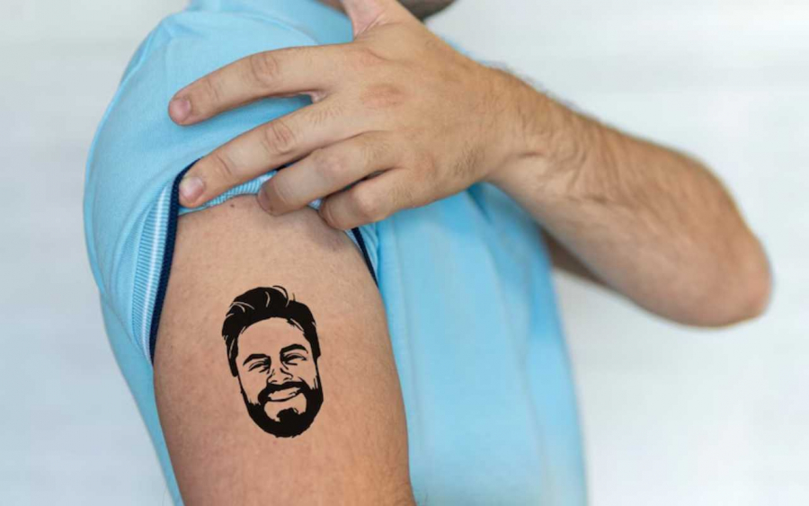 homem mostrando braço com tatuagem temporária com rosto do noivo usado em despedida de solteiro