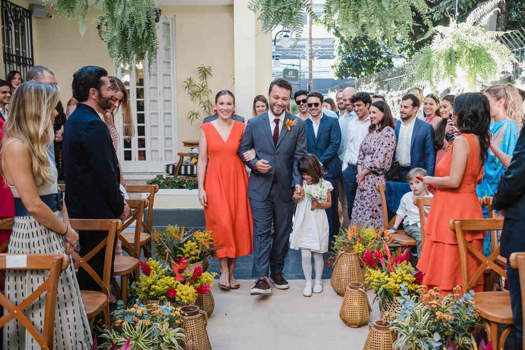 entrada do noivo ao lado de mulher com vestido laranja e menina com vestidinho branco