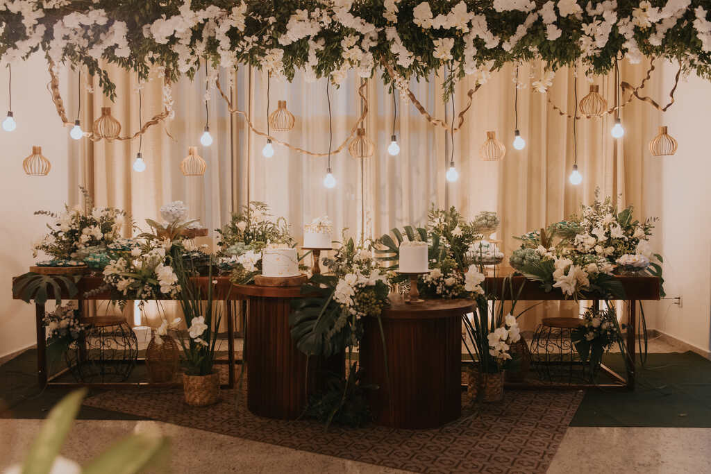 mesas de madeira com trio de bolos de casamento brancos com arranjos com flores brancas e costelas de adão