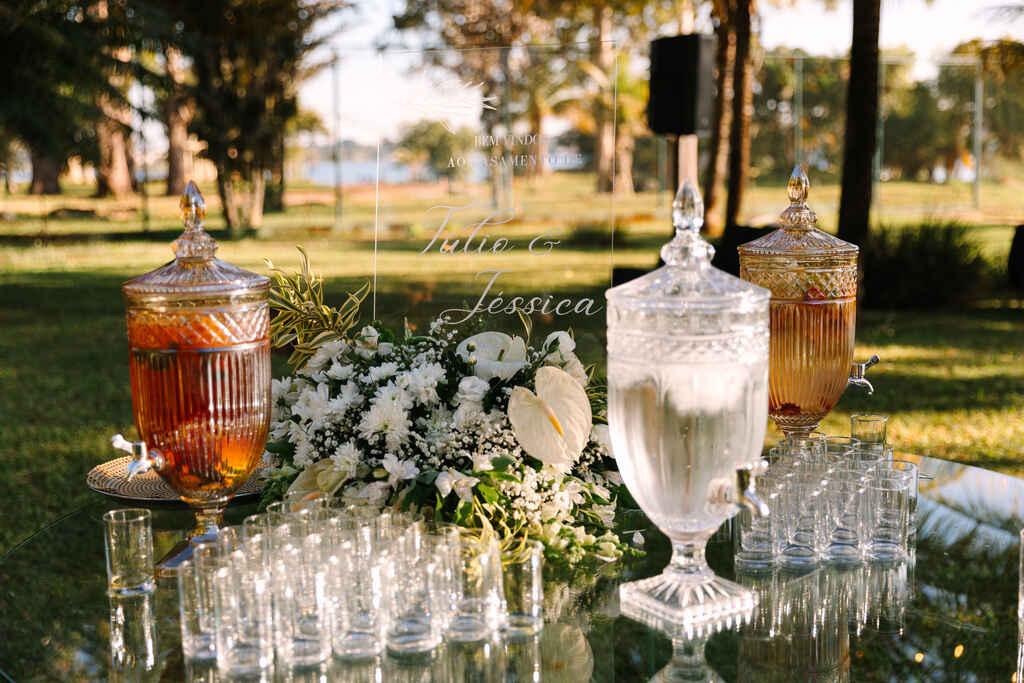 mesa de vidro com três suqueiras e arranjo de flores brancas ao lado de copos