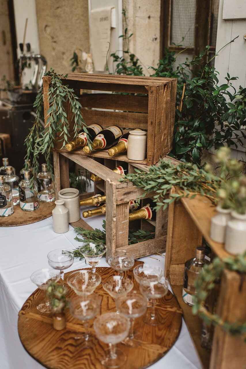 mesa com toalha branca e caixotes de madeira com garrafas de bebida e ramos de folhas decorativas