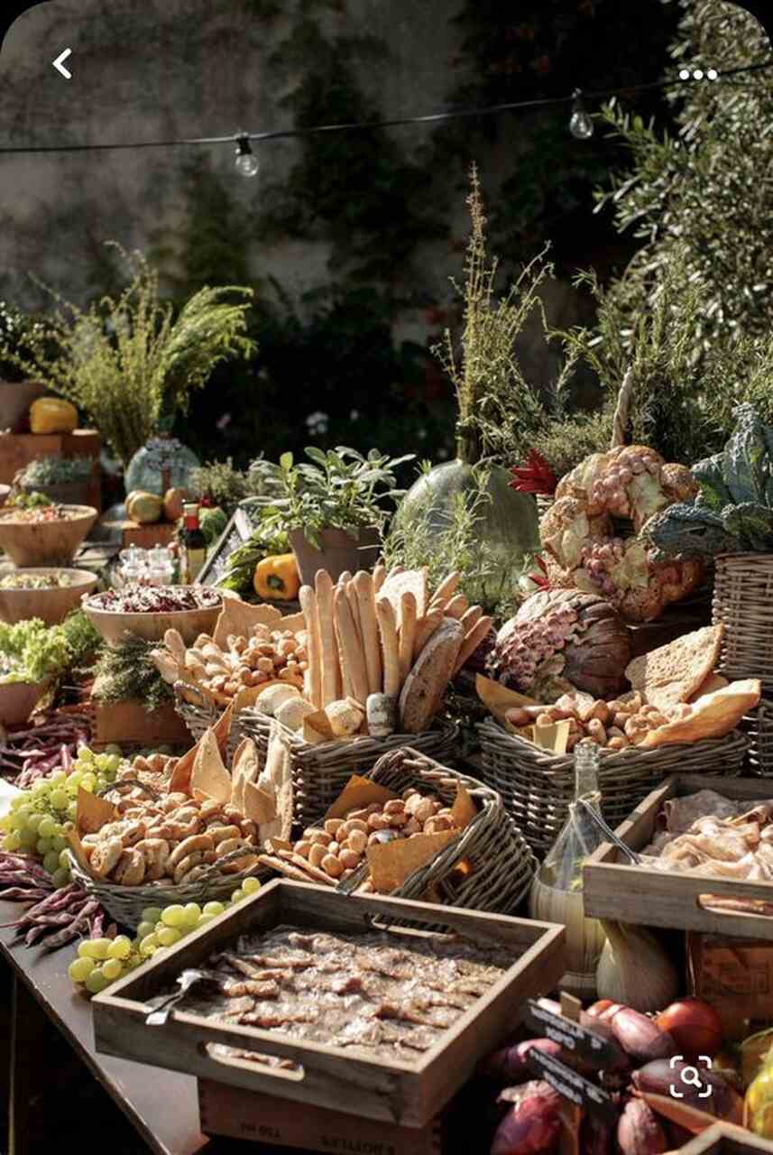 mesa ao ar livre com várias cestas rústicas com pães frutas uvas e torradas