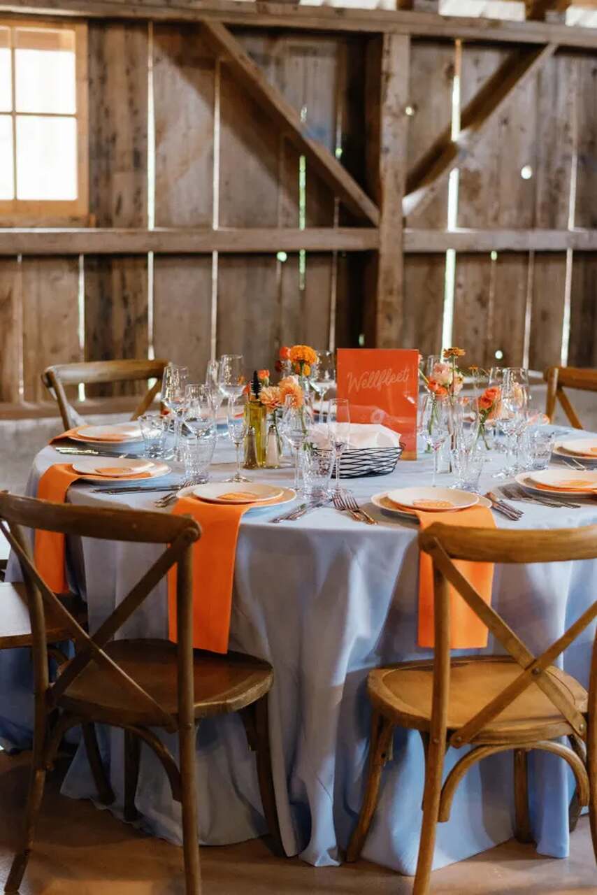 mesa posta com toalha branca e guardanapos laranja no salão rústico