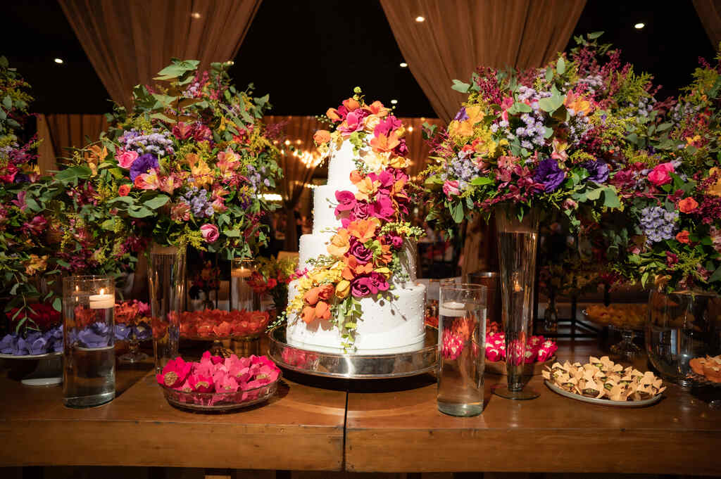 mesa de madeira com bolo de casamento e arranjos com flores coloridas