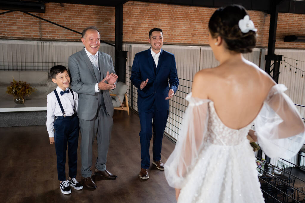 first look do pai da noiva com terno cinza ao lado de homem com terno azul e pajem com calça suspensório e gravata borboleta azul marinho