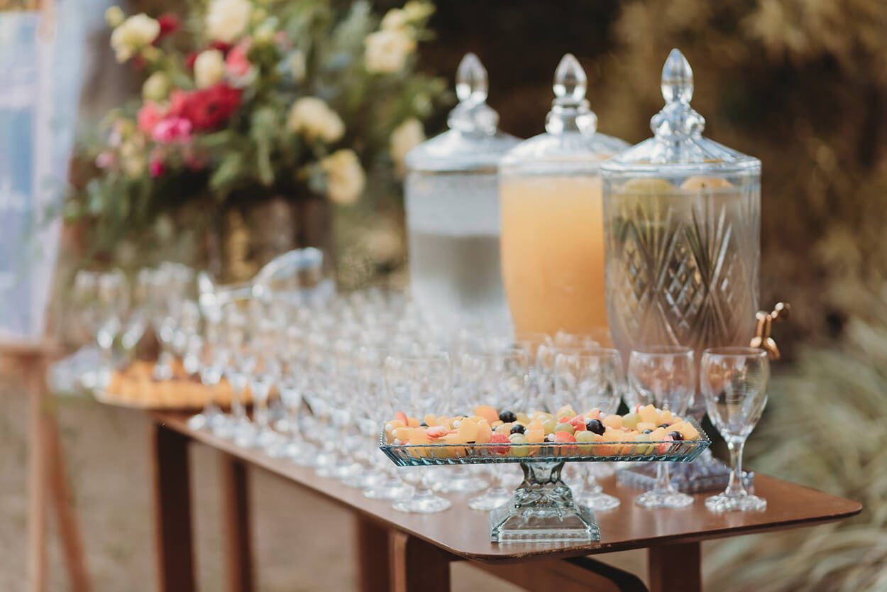 mesa de madeira com três suqueiras de vidro taças e bandejas com frutas