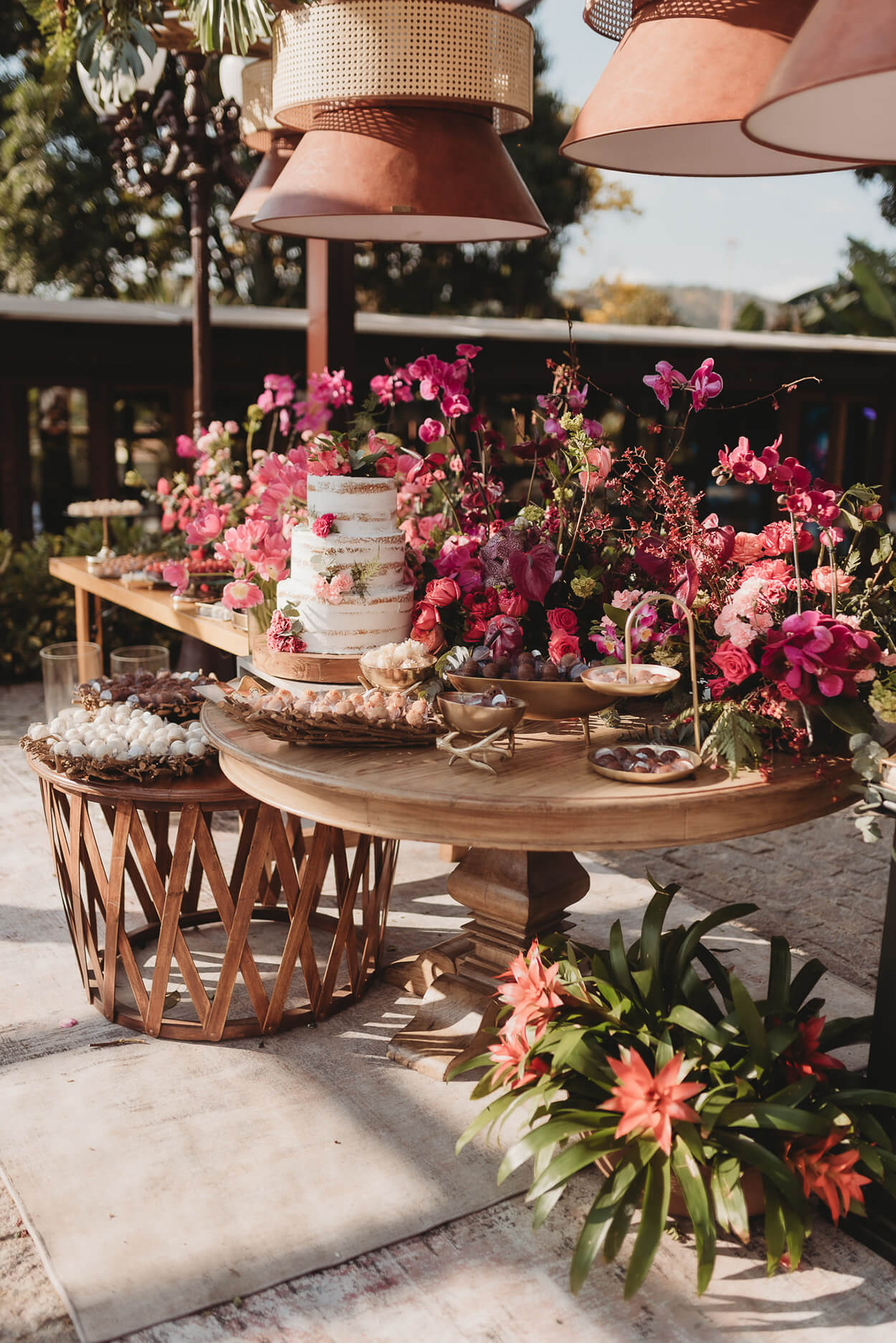 mesas de madeira com bolo de casamento semi espatulado com tres andares e arranjos de flores cor de rosa ao ar livre