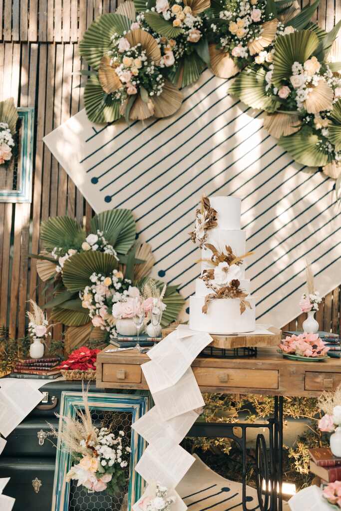 mesa de madeira rústica com bolo de casamento branco com três andares e flores secas no topo