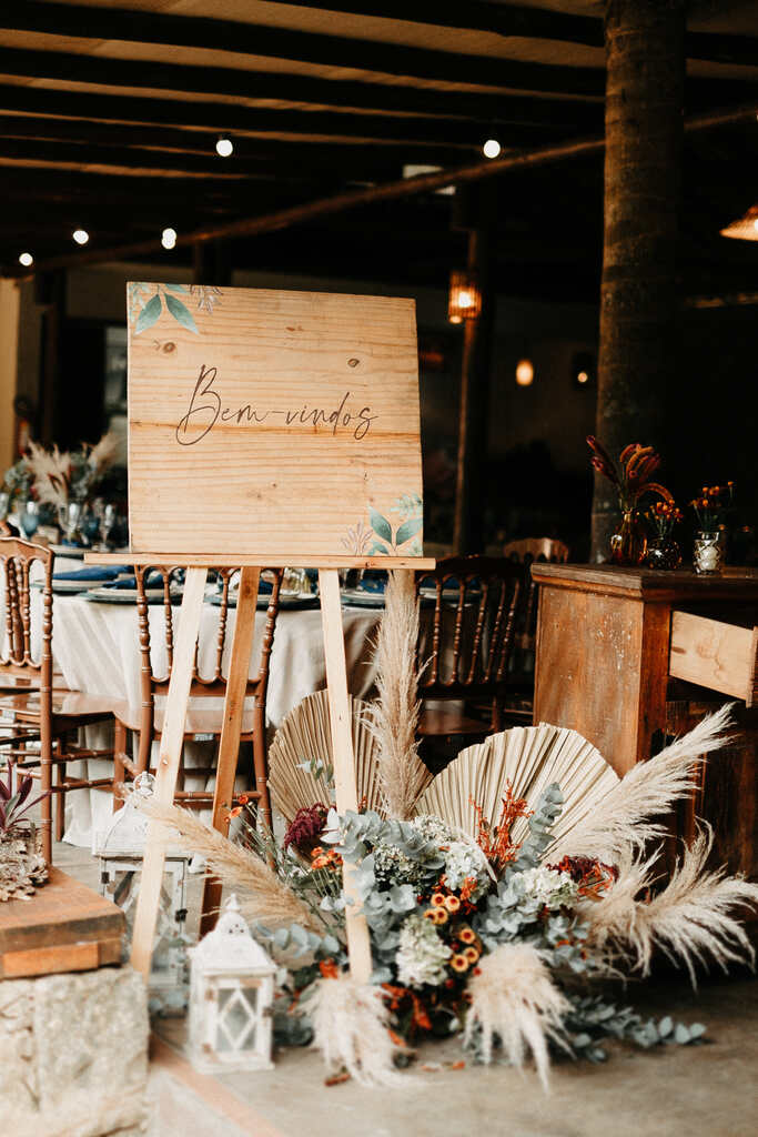 cavalete com placa escrito bem-vindos com vaso de flores com capim dos pampas e folhas secas