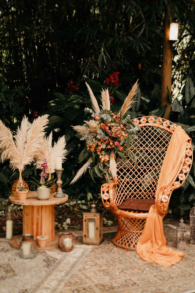 cadeira pavão com tecido e arranjo com flores secas e capim dos pampas e ao lado de mesa de madeira com vasos com capim dos pampas